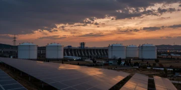 Paisaje energético europeo al atardecer con paneles solares, tanques de almacenamiento industrial y presa hidroeléctrica