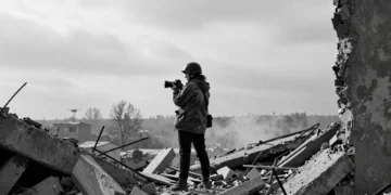 Fotoperiodista femenina entre escombros de edificio bombardeado en el Donbás, Ucrania, sosteniendo una cámara DSLR