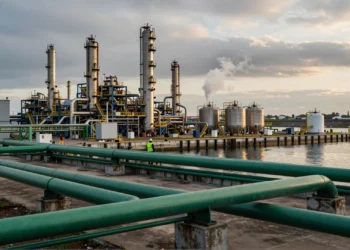 Biorrefinería industrial a orillas de un puerto europeo con tuberías verdes y un trabajador en pasarela