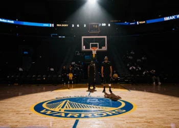Cancha vacía del estadio NBA de Golden State Warriors iluminada por un foco solitario con dos siluetas al fondo