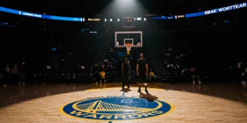 Cancha vacía del estadio NBA de Golden State Warriors iluminada por un foco solitario con dos siluetas al fondo