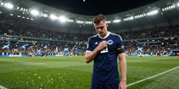 Andy Robertson con el brazalete de capitán de Escocia, cabizbajo en señal de duelo y determinación en un estadio lleno