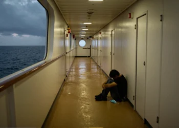 Pasillo vacío de crucero con iluminación tenue, figura solitaria sentada en el suelo y mascarilla desechada cerca