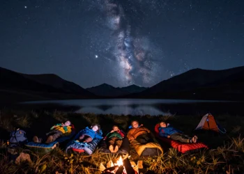 Familia con tres hijos durmiendo en sacos de dormir bajo un cielo estrellado en un prado alpino de montaña