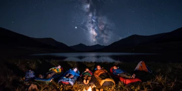 Familia con tres hijos durmiendo en sacos de dormir bajo un cielo estrellado en un prado alpino de montaña