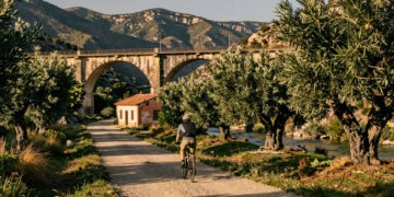 Ciclista en una vía verde española sobre antigua línea de ferrocarril, con viaducto de piedra y estación rural abandonada