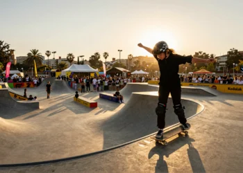 Joven skater femenina en truco sobre halfpipe en festival de deportes urbanos al atardecer en Barcelona