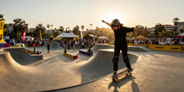 Joven skater femenina en truco sobre halfpipe en festival de deportes urbanos al atardecer en Barcelona