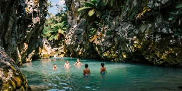 Grupo de personas refrescándose en una poza natural de agua turquesa en un estrecho cañón de roca caliza en Cataluña