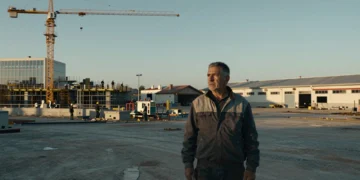 Trabajador español contempla el contraste entre una fábrica moderna activa y un polígono industrial abandonado