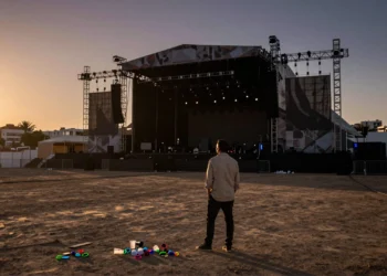 Promotor de espaldas observa un escenario vacío al atardecer en Valencia, entre restos de un festival de música cancelado