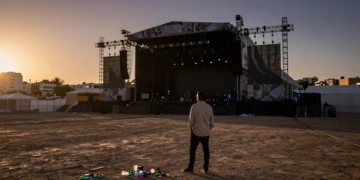 Promotor de espaldas observa un escenario vacío al atardecer en Valencia, entre restos de un festival de música cancelado