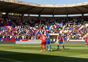Derbi regional murciano en Primera Federación: dos jugadores disputan un balón aéreo ante una grada repleta de aficionados