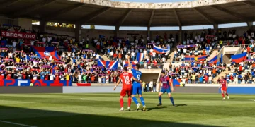 Derbi regional murciano en Primera Federación: dos jugadores disputan un balón aéreo ante una grada repleta de aficionados