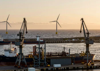 Astillero industrial en la costa asturiana al atardecer con aerogeneradores marinos flotantes en el horizonte del Atlántico