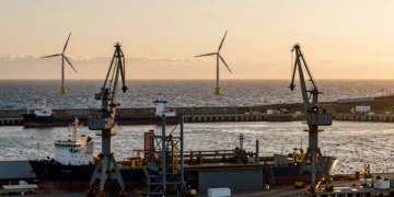 Astillero industrial en la costa asturiana al atardecer con aerogeneradores marinos flotantes en el horizonte del Atlántico