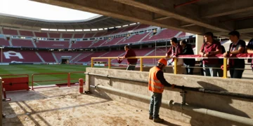Obras de renovación en el estadio Enrique Roca del Real Murcia con obreros, andamios y aficionados observando