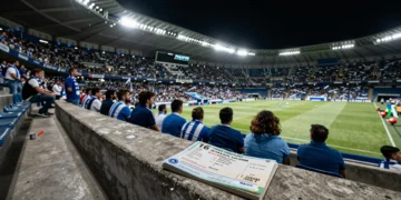 Abono de temporada y recibo sobre un asiento del estadio Riazor con aficionados del Deportivo al fondo