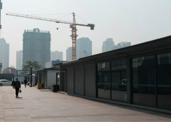 Calle comercial vacía en ciudad china con negocios cerrados, grúa inactiva y peatones bajo cielo gris nublado
