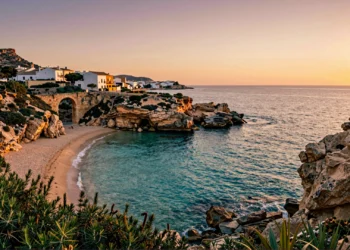 Cala mediterránea virgen en Murcia al atardecer, con acantilados de caliza, arco romano y pueblo pesquero de paredes blancas