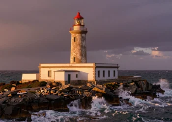 Faro español histórico sobre acantilados atlánticos al atardecer, con luz dorada y olas rompiendo en rocas