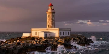Faro español histórico sobre acantilados atlánticos al atardecer, con luz dorada y olas rompiendo en rocas