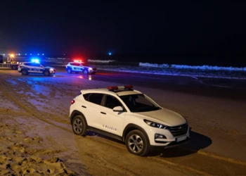 SUV blanco varado en la arena mojada de una playa española de noche con coches de policía local y luces de emergencia