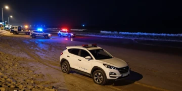 SUV blanco varado en la arena mojada de una playa española de noche con coches de policía local y luces de emergencia