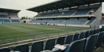 Gradas casi vacías del estadio del Lorca Deportiva con un abono de temporada arrugado sobre un asiento de plástico