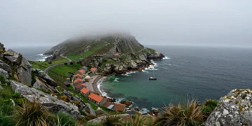 Costa atlántica de las Rías Altas de Galicia con acantilados de granito, aldea pesquera y barca solitaria en aguas esmeralda
