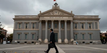Congreso de los Diputados en Madrid bajo cielo gris otoñal con hojas caídas y funcionario cruzando la plaza