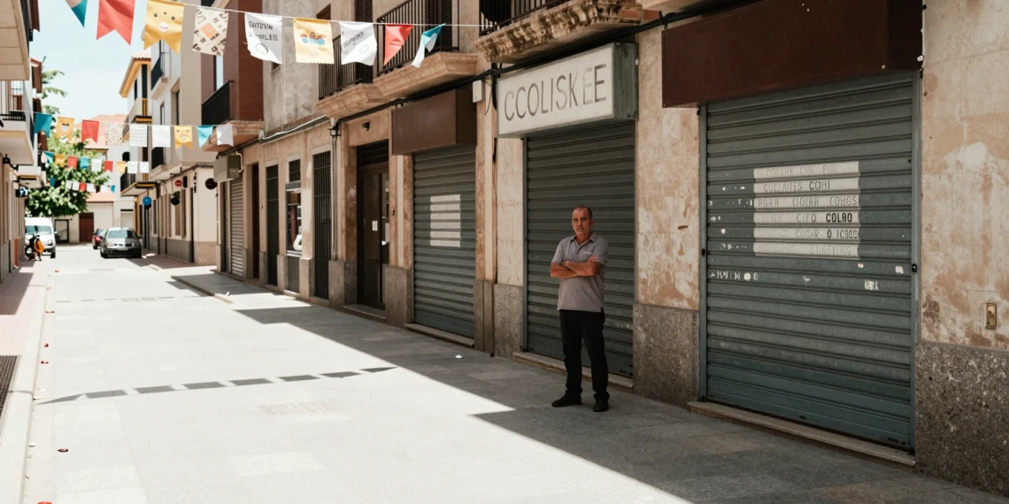 Empresario ceuti con brazos cruzados frente a comercios cerrados en calle desierta durante la temporada de verano