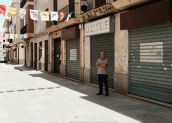 Empresario ceuti con brazos cruzados frente a comercios cerrados en calle desierta durante la temporada de verano