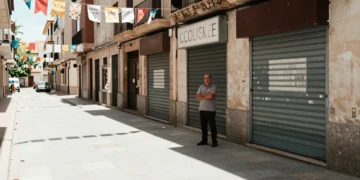 Empresario ceuti con brazos cruzados frente a comercios cerrados en calle desierta durante la temporada de verano
