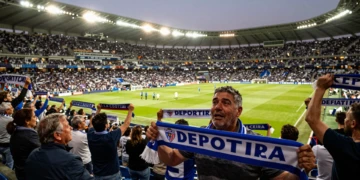 Aficionado del Deportivo de La Coruña emocionado con bufanda azul y blanca en estadio lleno en el regreso a LaLiga