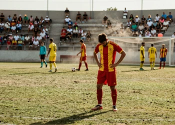 Futbolista cabizbajo con camiseta roja y amarilla en partido de pretemporada del fútbol catalán