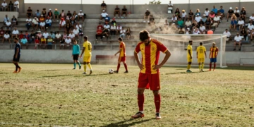 Futbolista cabizbajo con camiseta roja y amarilla en partido de pretemporada del fútbol catalán