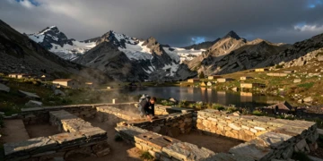 Arqueólogo excavando artefactos prehistóricos junto a un lago glaciar en los Pirineos catalanes al atardecer