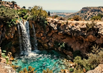 Cascada travertina de tres metros con poza turquesa en un cañón de la Región de Murcia, con senderista al fondo