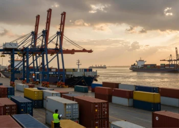 Puerto comercial al atardecer con grúas de carga, buques mercantes y contenedores de envío europeos apilados en el muelle