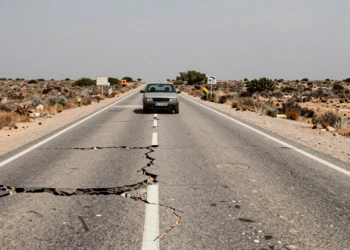Carretera secundaria española con asfalto agrietado y baches profundos en paisaje rural seco y abandonado