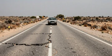 Carretera secundaria española con asfalto agrietado y baches profundos en paisaje rural seco y abandonado