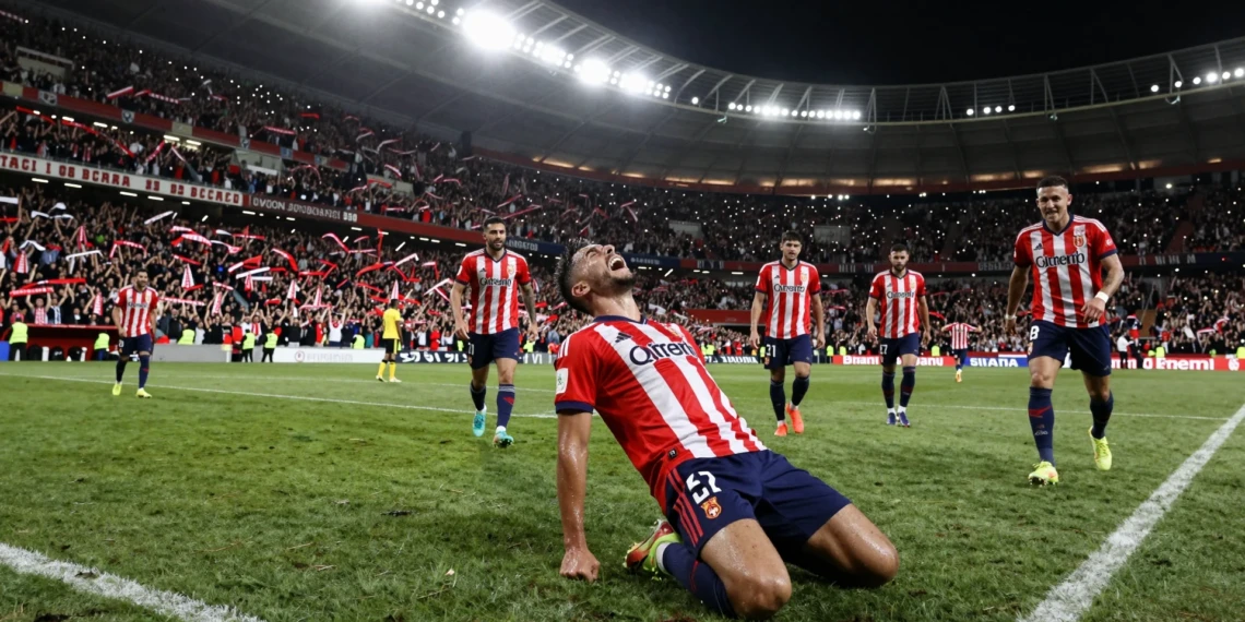 Jugador del Sevilla de rodillas celebrando un gol agónico ante su afición en el estadio bajo los focos nocturnos