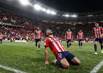 Jugador del Sevilla de rodillas celebrando un gol agónico ante su afición en el estadio bajo los focos nocturnos