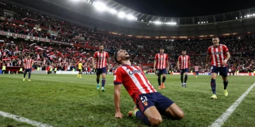 Jugador del Sevilla de rodillas celebrando un gol agónico ante su afición en el estadio bajo los focos nocturnos