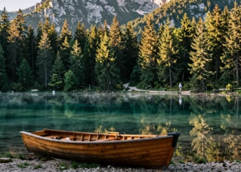Mujer contemplando un lago alpino de aguas turquesas en Eslovenia al amanecer, con un bote de madera en la orilla