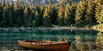 Mujer contemplando un lago alpino de aguas turquesas en Eslovenia al amanecer, con un bote de madera en la orilla