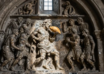 Figura condenada mordiendo una empanada en el Pórtico de la Gloria de Santiago de Compostela, talla románica de 1188
