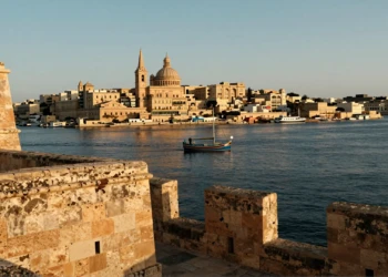 Vista del Gran Puerto de La Valeta al amanecer con murallas de piedra caliza dorada y un luzzu tradicional maltés