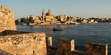 Vista del Gran Puerto de La Valeta al amanecer con murallas de piedra caliza dorada y un luzzu tradicional maltés